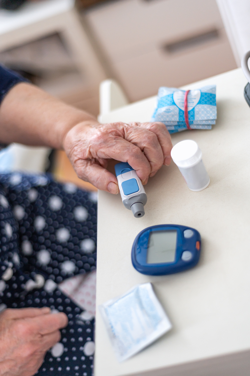 Senior Woman tests blood for glucose or sugar level for diabetes with glucometer, close up of hands, home kit for testing